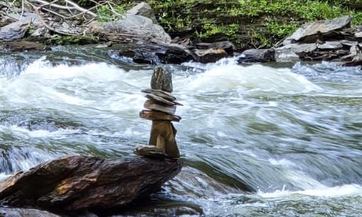 Balanced tower of rocks standing still beside a waterfall